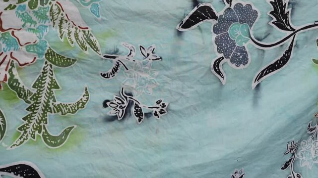 Cinematic close-up of handmade Indonesian batik fabric showing colorful floral motif on light blue textile.