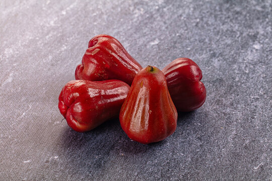 Four red wax apples resting on grey stone surface, tropical fruit pile