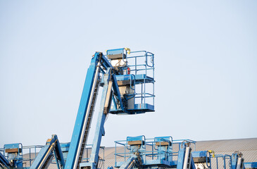 Blue boom lifts with raised work platforms against a clear sky, with empty guardrailed baskets and extended booms above parked equipment in daylight, leaving ample copy space around the machinery © Fahroni