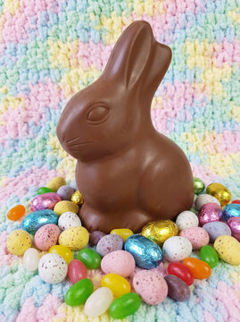 Chocolate Easter bunny surrounded by colorful candy eggs on pastel background