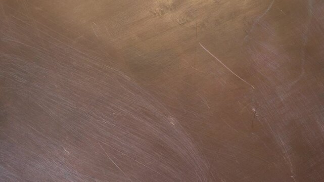 Copper sheet reflecting light creates an abstract textured background for use in design projects. Soft, warm light illuminates the copper surface texture. 