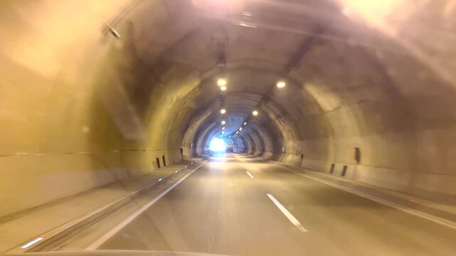 The moment of exiting a highway tunnel illuminated by an in-car camera, the tunnel exit, and daylight.