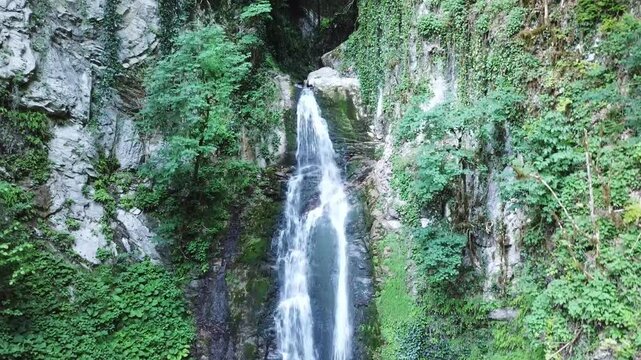 Aerial top view of the majestic Azhek Waterfall cascading down a steep rocky cliff surrounded by lush green forests in Sochi, Russia.