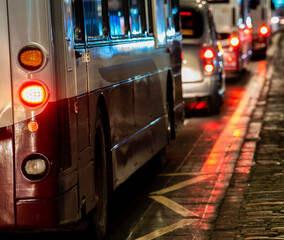 Rear of a city bus with glowing tail lights in queuing evening traffic on a wet cobbled street © Scott