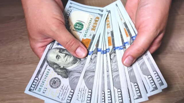 Close-up video of hands holding flipping through stack of hundred dollar bills estimating amount enjoying feeling of financial wealth success abundance Slow motion video Business transactions planning