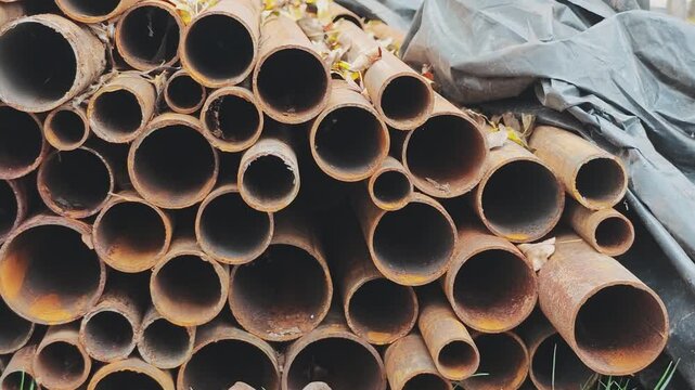 Stack of rusty steel pipes stored outdoors in industrial yard, showcasing weathered texture and circular patterns