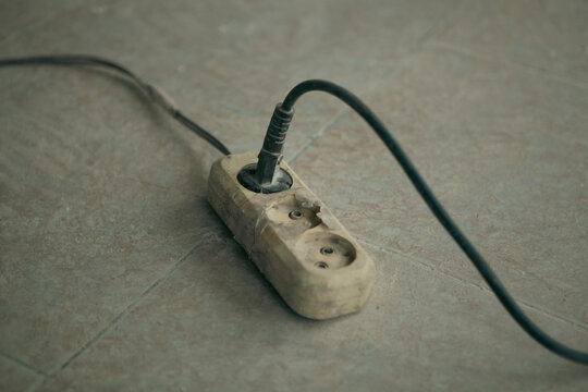 Electric plug and socket on a tile floor. Old electrical outlet.