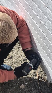 Home repair handyman using an electric screwdriver to attach wooden paneling to a house frame outdoors. High-angle static close-up shot.
