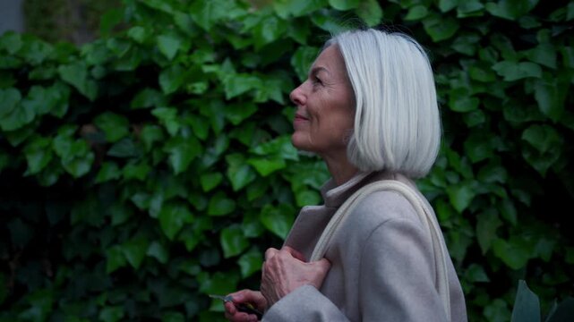 Video of stylish mature woman with gray hair on city street, enjoying beautiful weater during free weekend day.