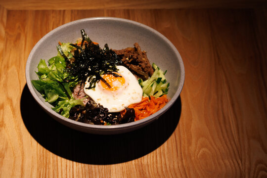 Grilled meat, egg, greens, and vegetables in a bowl