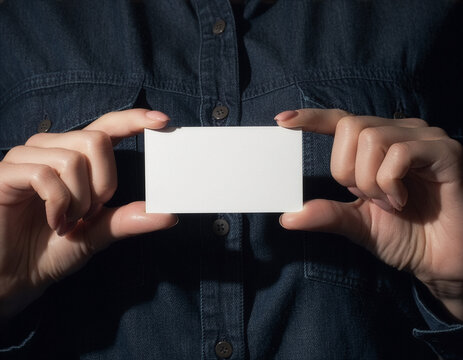 Blank white business card mockup held in front of a dark denim shirt