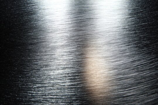 A close-up view reveals a textured brushed metal surface with parallel lines. This abstract background is ideal for industrial or modern graphic projects.