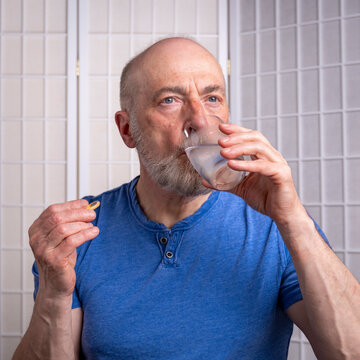 senior man is taking a medicine or supplement pill with a glass of water at home, self care health concept
