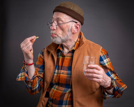 senior man is looking with disgust and doubt at a medicine or supplement pill to swallow, self care health concept