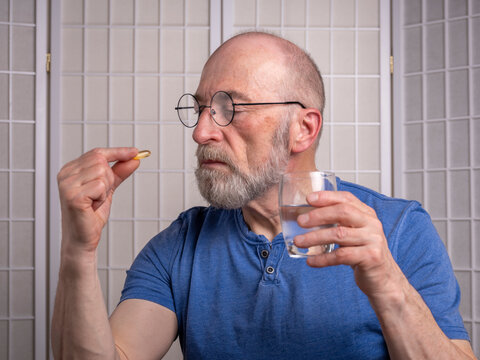 senior man is taking a medicine or supplement pill with a glass of water at home, self care health concept