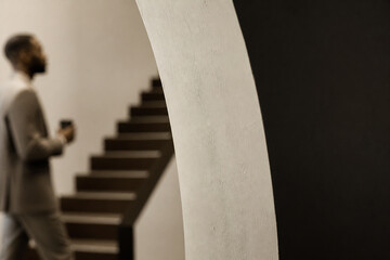 Fototapeta premium A man stands near a staircase next to a large white architectural column in an indoor, minimalist setting.