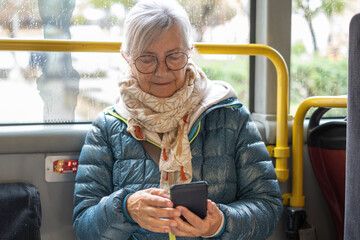 Senior adult woman in public transit using smartphone, staying connected and enjoying modern technology while commuting on a city bus © luciano