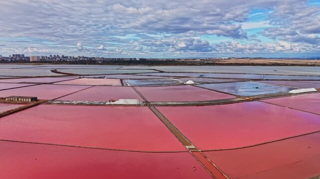 Salt extraction takes place in shallow ponds divided by narrow paths, with red and pink water stretching toward a settlement on the horizon during the day.