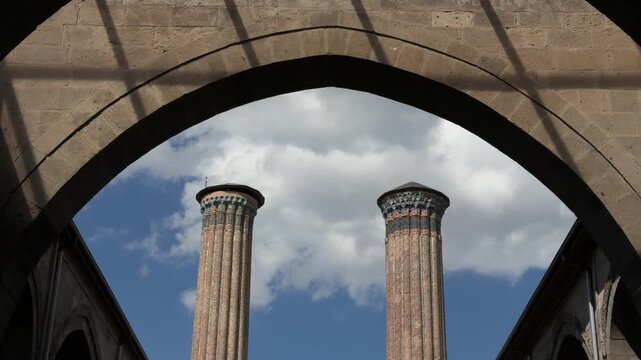 &Ccedil;ifte Minareli Medrese. Historic stone courtyard framed by Gothic arches with twin brick chimneys beneath a bright blue sky, architectural heritage view
