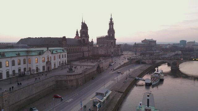 Aerial drone flight over Dresden Germany cityscape featuring the historic Hofkirche Elbe River Augustus Bridge and Br&uuml;hls Terrace with pedestrians at dusk