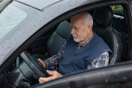 Older man sits behind the steering wheel of a car during rainy weather