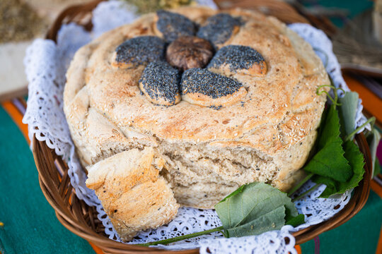 Traditional round harvest bread decorated with poppy seed flower motif served in a wicker basket with lace during Polish thanksgiving.