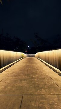 illuminated modern pathway in Benchakitti park at night, stylish bridge entrance or walkway glowing over serene landscape, 4k vertical video