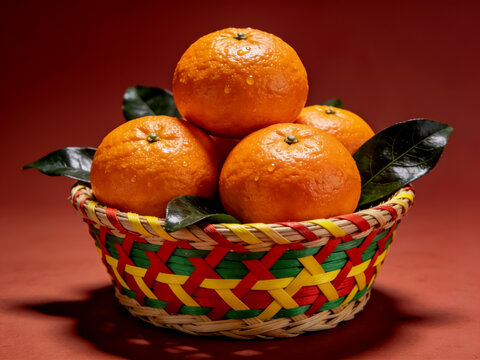 Fresh orange tangerines with green leaves in a colorful woven basket on red