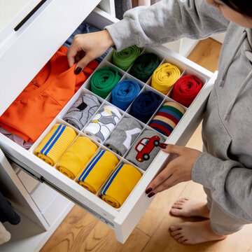 Person organizing colorful folded socks and clothes inside a white bedroom dresser drawer