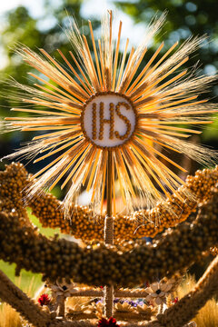 Close up of a harvest wreath featuring a radiating IHS monogram symbol intricately crafted from golden wheat ears.