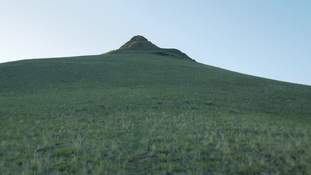 Green Grassy Hillside Ascending to a Distinct Rocky Mountain Peak Under Clean Blue Sky in Khakassia