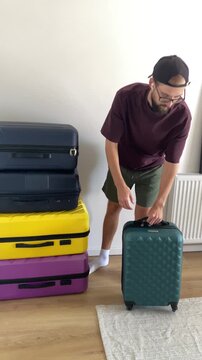 Young man takes a green suitcase from a stacked pile of colorful luggage and rolls it away