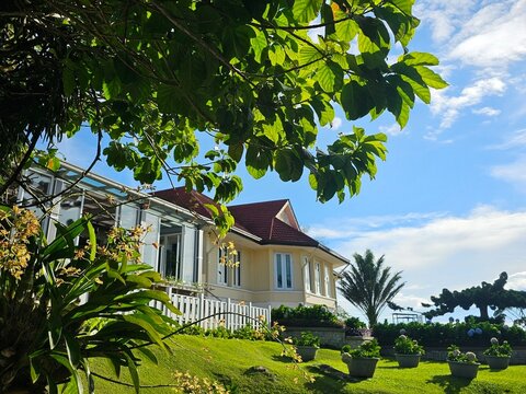 Beautiful highland resort hotel on a green hill slope with a bright blue sky, framed by lush green trees.