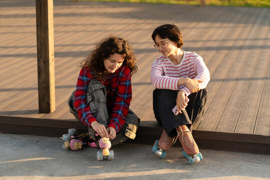 Two women lacing up roller skates at an outdoor rink
