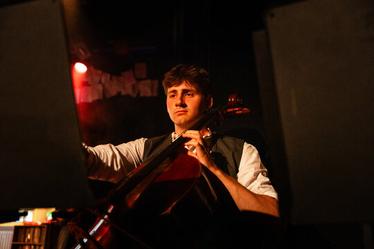 A cellist plays with focused intensity beneath a red glow