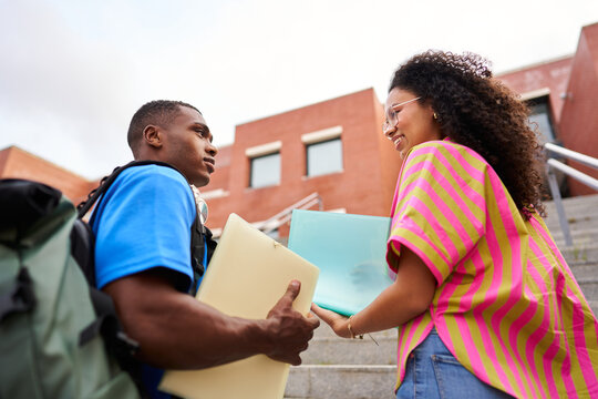University students conversing on campus stairs holding folders