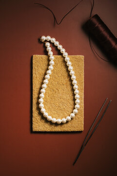 Spool of thread, tweezers and pearl necklace on rectangular sponge
