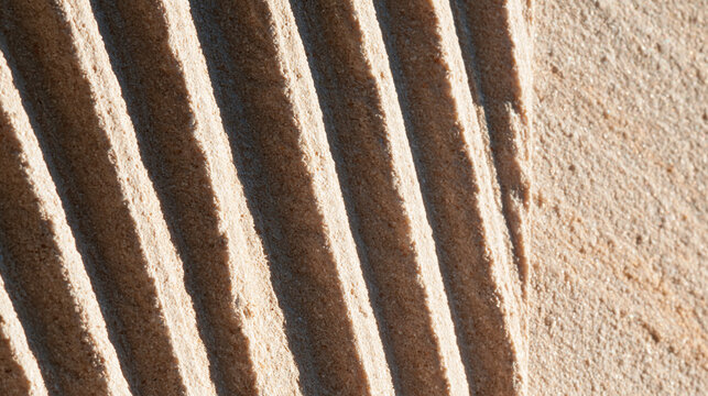 Macro texture of carved parallel grooves in beige sandstone under hard light, in a realistic photographic style