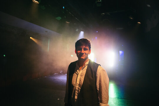 A performer smiles warmly amid glowing stage haze