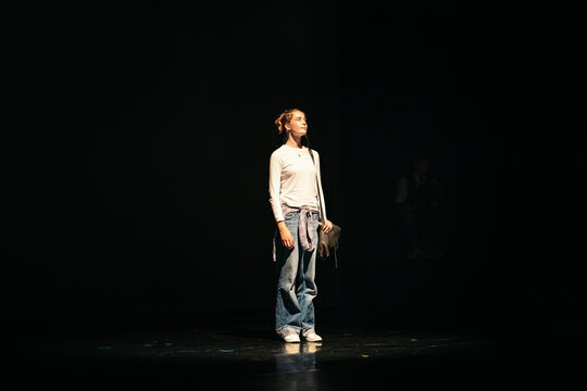 A solo performer stands illuminated on an empty stage
