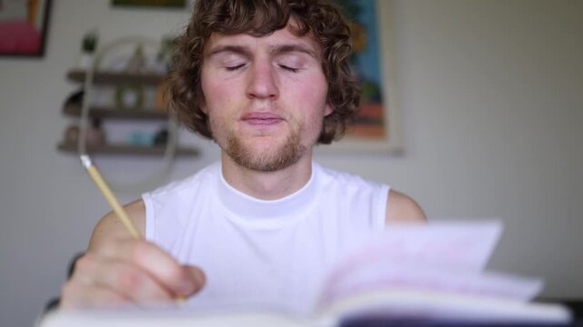 A weary young student stays up late preparing for exams with a notebook and a pen while struggling to focus and searching for answers during a late night of study at home