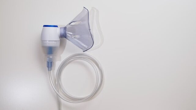Nebulizer. Top view on a inhaler with a blue mask on the white background. Inhalation concept, lung diseases in the upper respiratory tract. Copy space. High quality 4k footage.