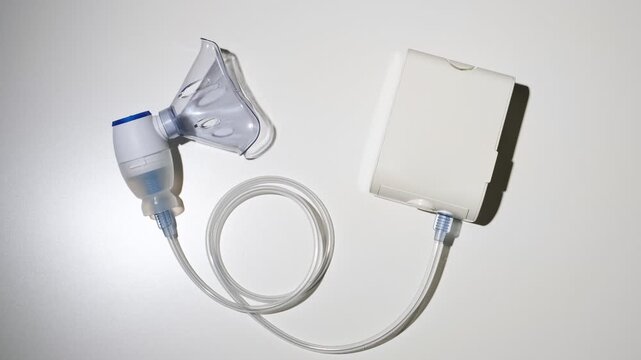 Nebulizer. Top view on the inhaler with a blue mask on the white background. Inhalation concept, lung diseases in the upper respiratory tract. High quality 4k footage.