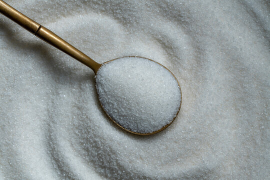 White sugar crystals texture with golden spoon. Granulated white sugar or sea salt full frame background. Brass spoon filled with sweet sugar crystals on textured background for bakery recipe