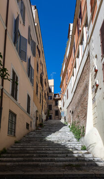 Narrow stone staircase between pastel buildings under a deep blue sky in the historic centre of Rome, Italy