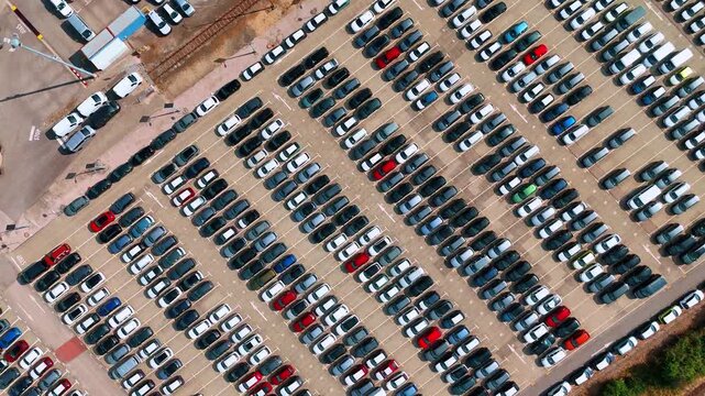 Parked vehicles form diagonal rows across a storage lot. White, black and red cars form repeated lines across a paved storage lot.