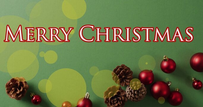 Displaying large text MERRY CHRISTMAS greeting on green cardstock, with pine cones and red baubles