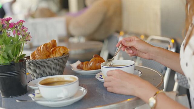 Woman stirring coffee beside croissants and pink flowers at Paris cafe