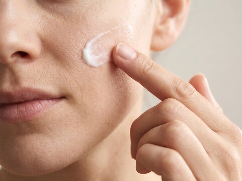 A woman applying moisturizing cream to her cheek with a fingertip in a close up view with finger smooth product