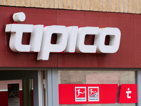 Germany, Husum, October 20. 2026, a Tipico sports betting shop storefront. red corporate banners, branding decals, and an image of the Bundesliga champion trophy (Meisterschale)